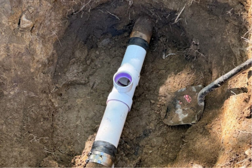 Top-down view of a newly installed or repaired outdoor white PVC sewer cleanout pipe in a dug-up trench.