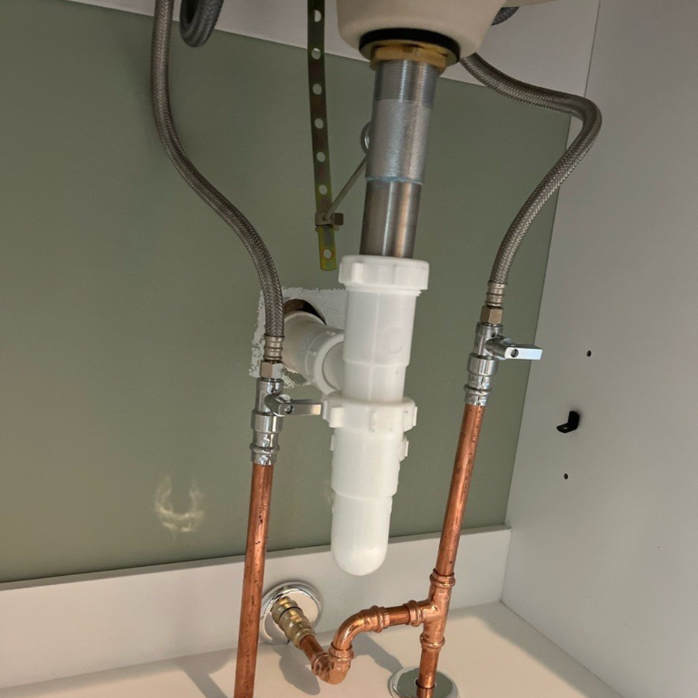 Close-up of a newly installed white P-trap and copper water lines under a bathroom vanity