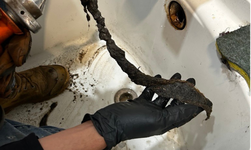 Professional plumber removing a massive hair clog from a bathtub drain using a drain snake.
