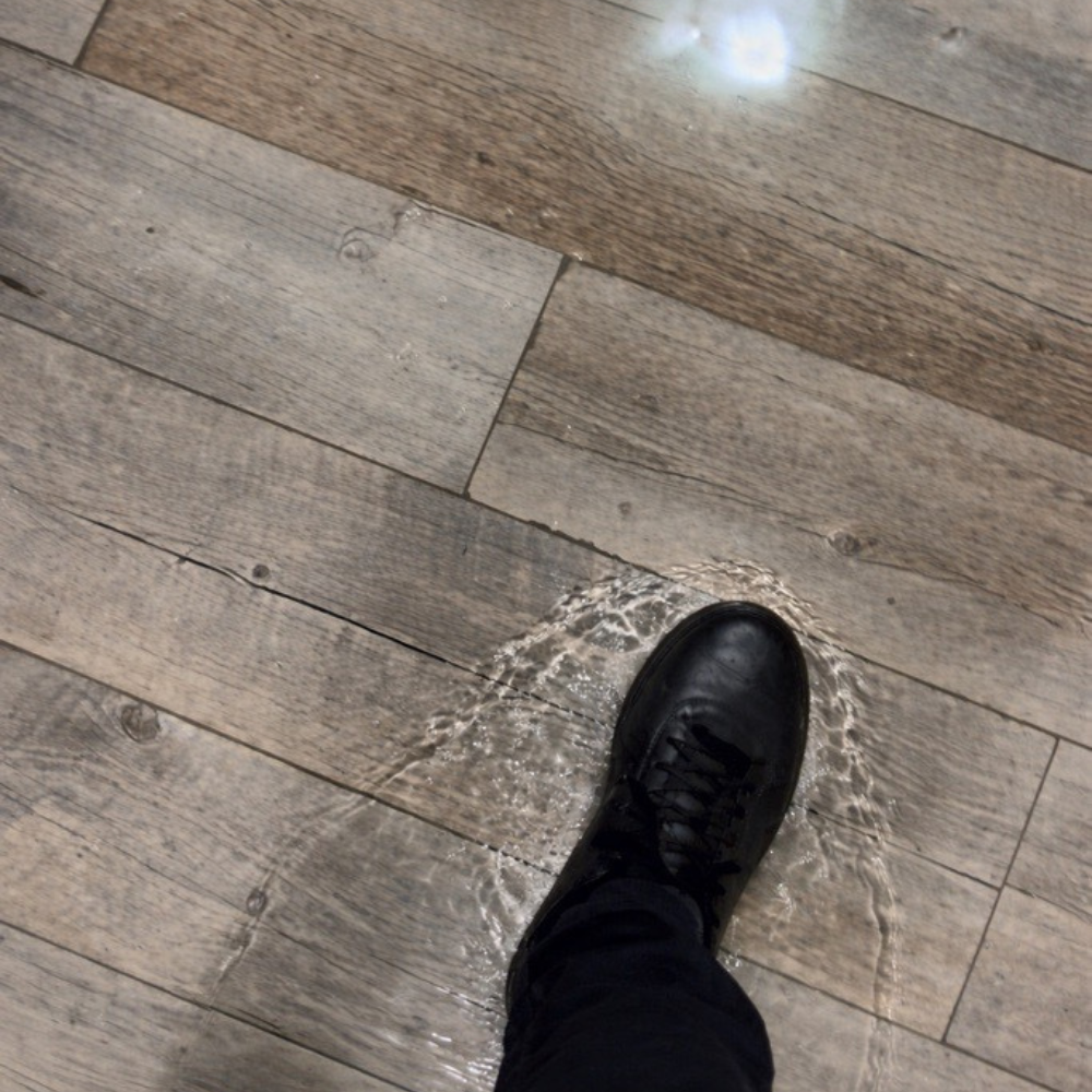 A foot stepping into a puddle of water on a floor, illustrating a common household plumbing leak.