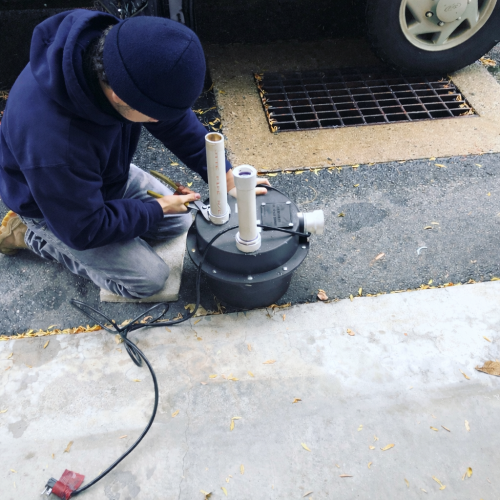 Plumber assembling a black sewage ejector pump basin with PVC pipes outdoors