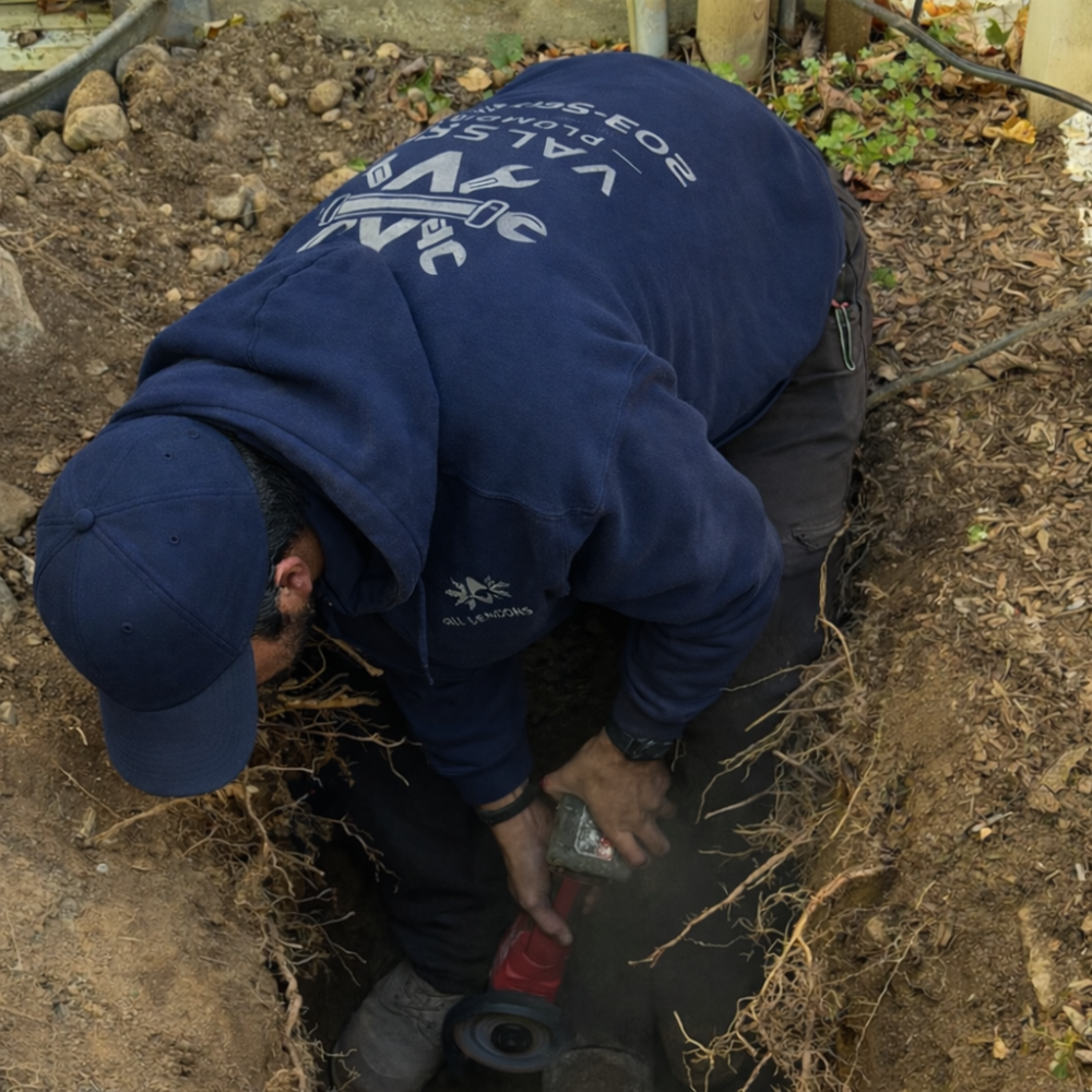 Emergency plumber performing excavation and pipe cutting for underground drain line repairs.